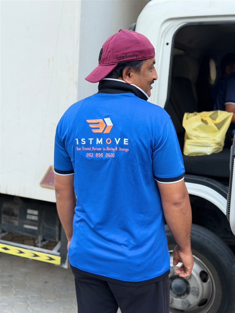 Real 1stMove crew member in a branded uniform standing beside a 1stMove moving truck in Dubai