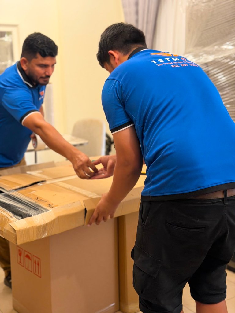 Two real 1stMove crew members taping a large moving box together indoors