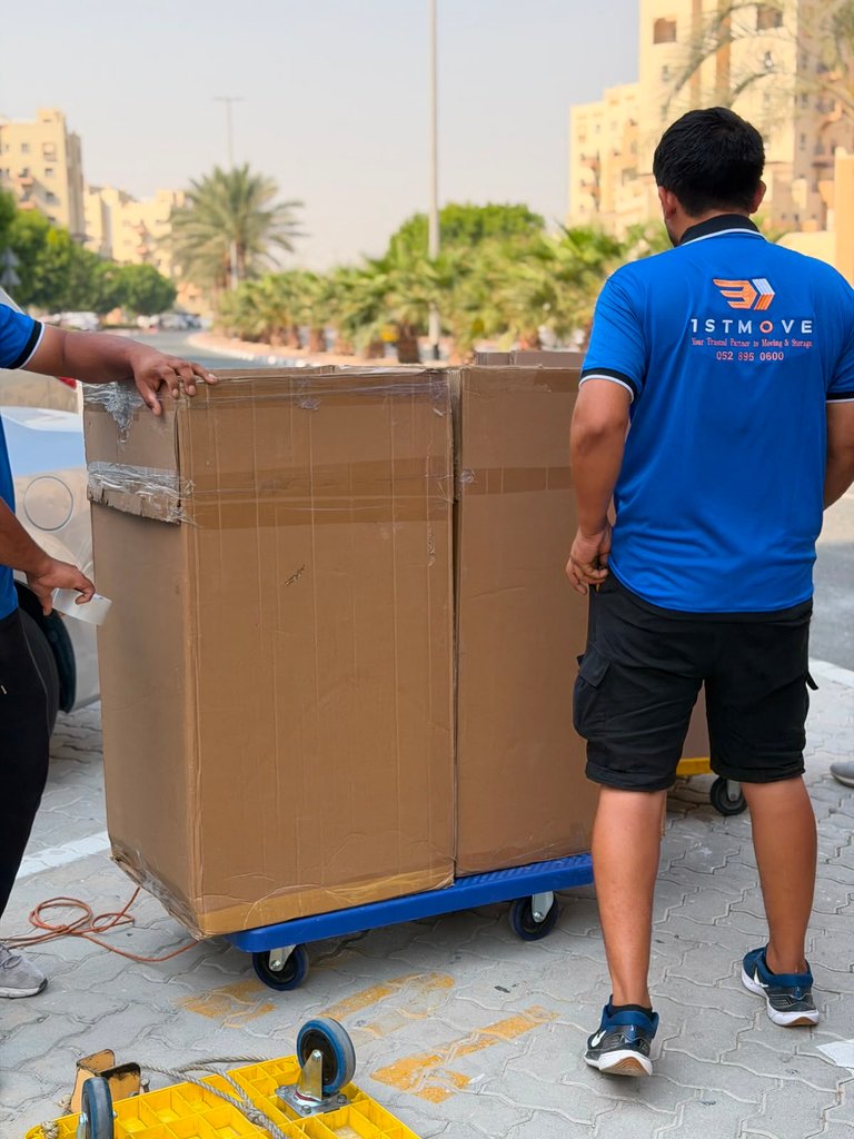 Real 1stMove crew member outdoors moving boxes on a dolly cart near mid-rise Dubai buildings