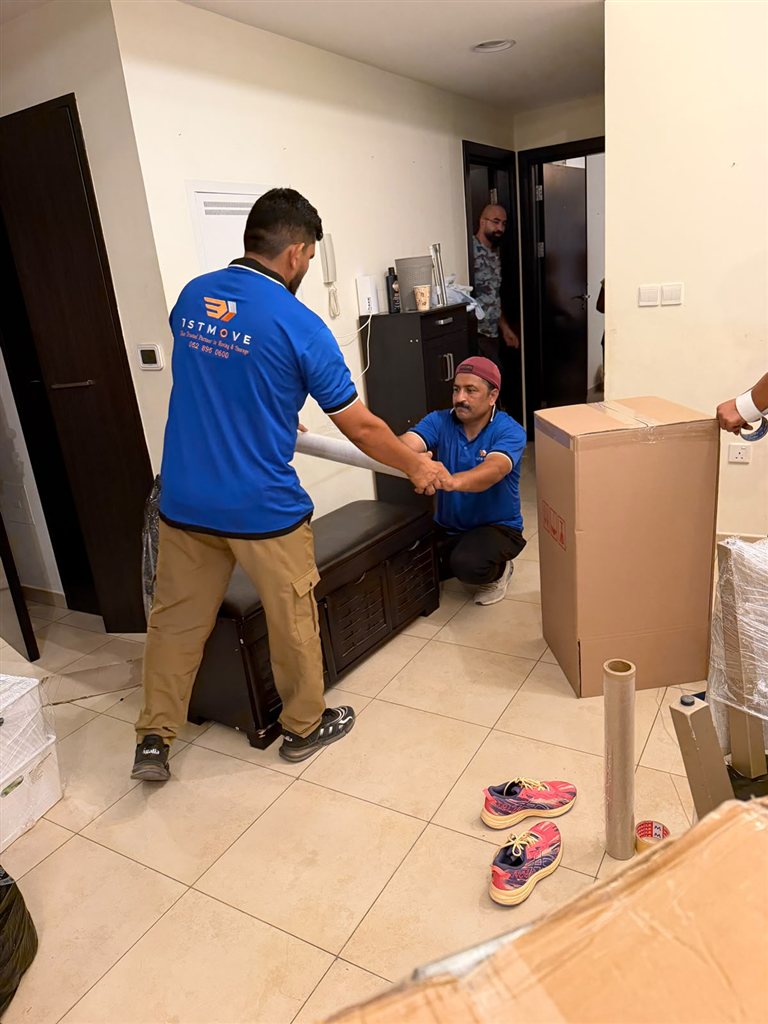 Real 1stMove crew member in a branded uniform carrying wrapped furniture during a move in Dubai