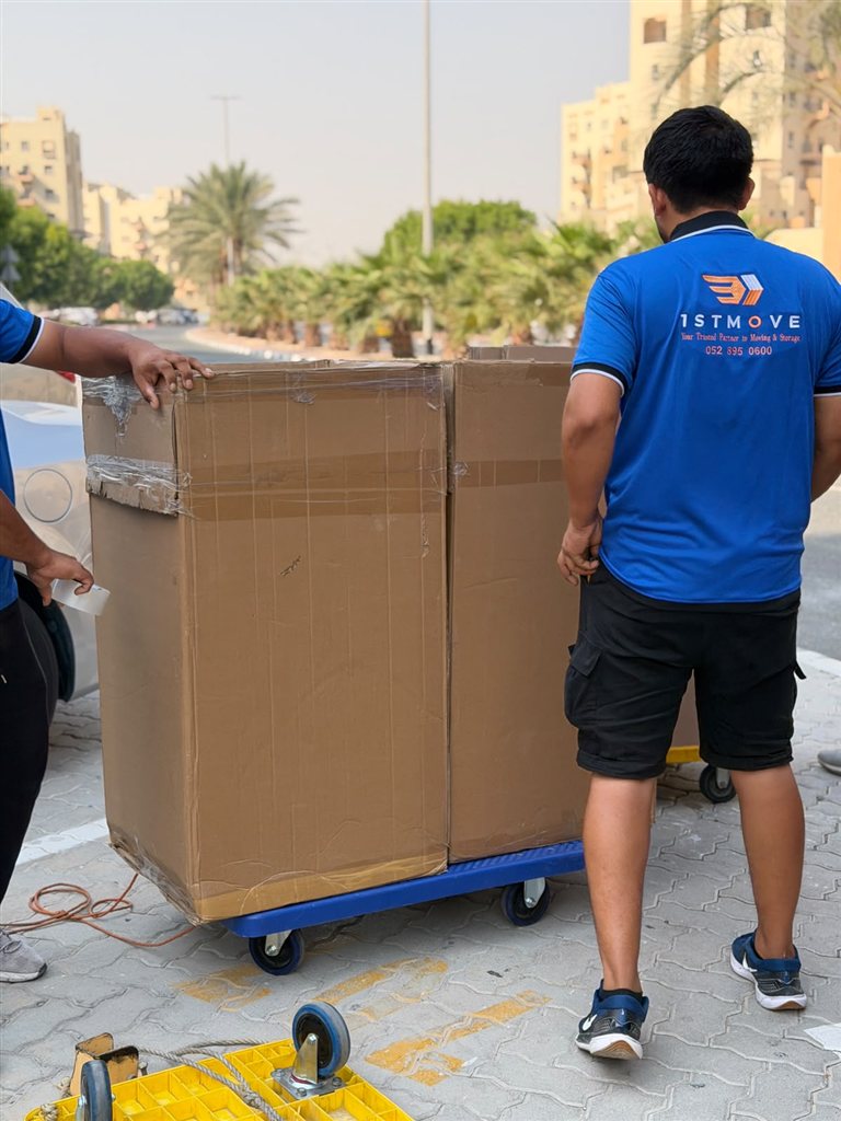 Real 1stMove crew members loading a wrapped box onto a trolley on a residential street