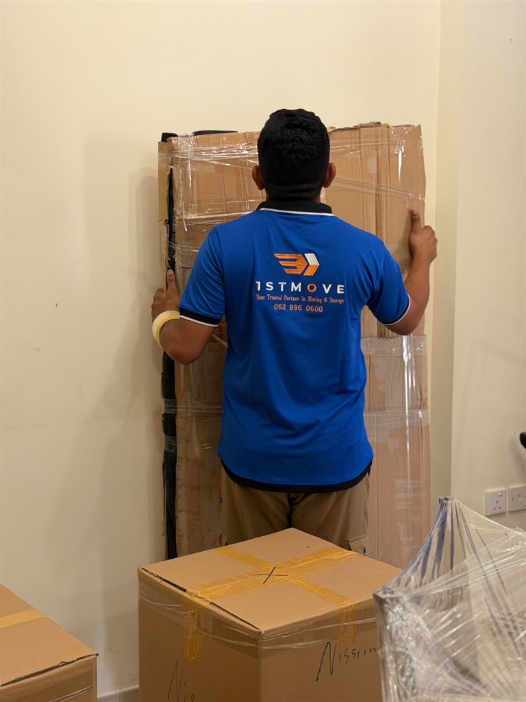 Real 1stMove crew member in a branded uniform wrapping and labeling boxes ready for storage in Dubai